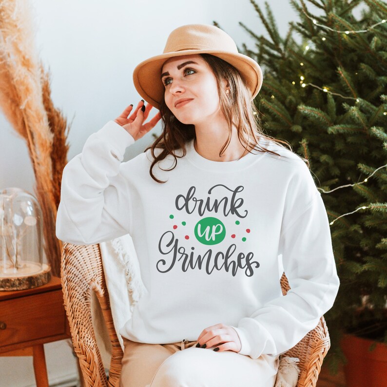 May include: White sweatshirt with the text "drink up Grinches" in gray script with green and red dots around the text.