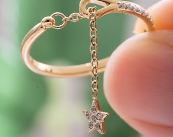 May include: A gold ring with a delicate chain and a star-shaped pendant. The star is set with small diamonds.