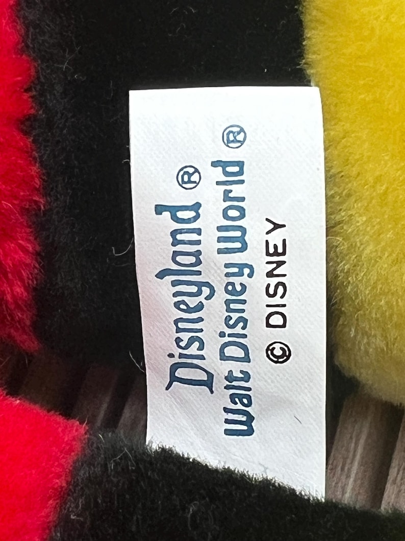 May include: White tag with black text that reads "Disneyland&reg; Walt Disney World&reg; &copy; DISNEY".