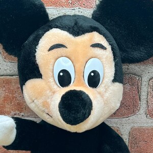 May include: A plush Mickey Mouse toy with black ears, a black nose, and large white eyes. The toy is wearing red shorts with a yellow button.