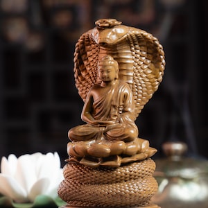 May include: A wooden sculpture of Buddha seated in meditation, with a cobra hood behind him. The sculpture is carved with intricate details and is a beautiful example of traditional Buddhist art.