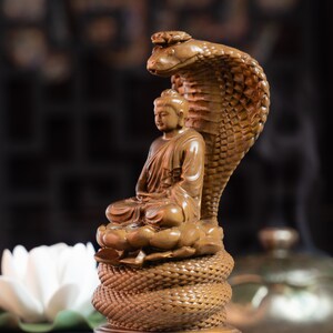 May include: A wooden sculpture of Buddha seated on a coiled cobra, with the cobra's head raised above Buddha's head.