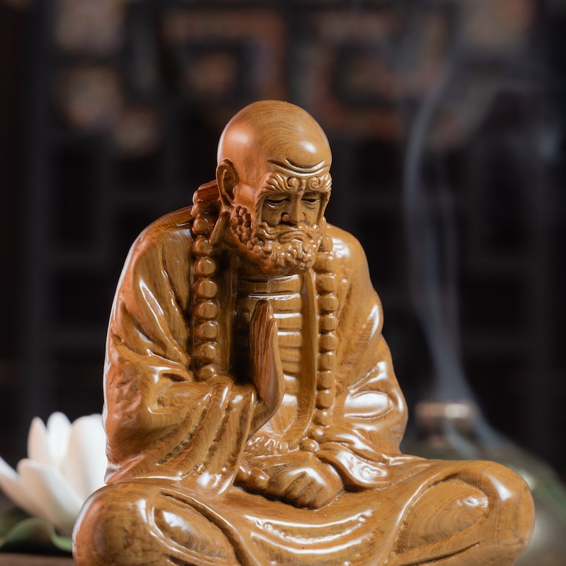 May include: A wooden statue of a meditating figure with a long beard and a beaded necklace. The statue is carved in a detailed style and has a warm brown color.