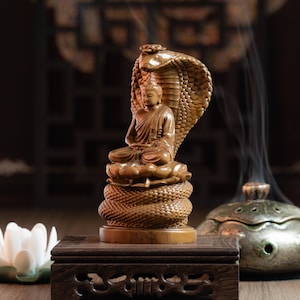 May include: A wooden sculpture of Buddha seated on a coiled snake, with a lotus flower base. The sculpture is on a wooden platform with intricate carvings.
