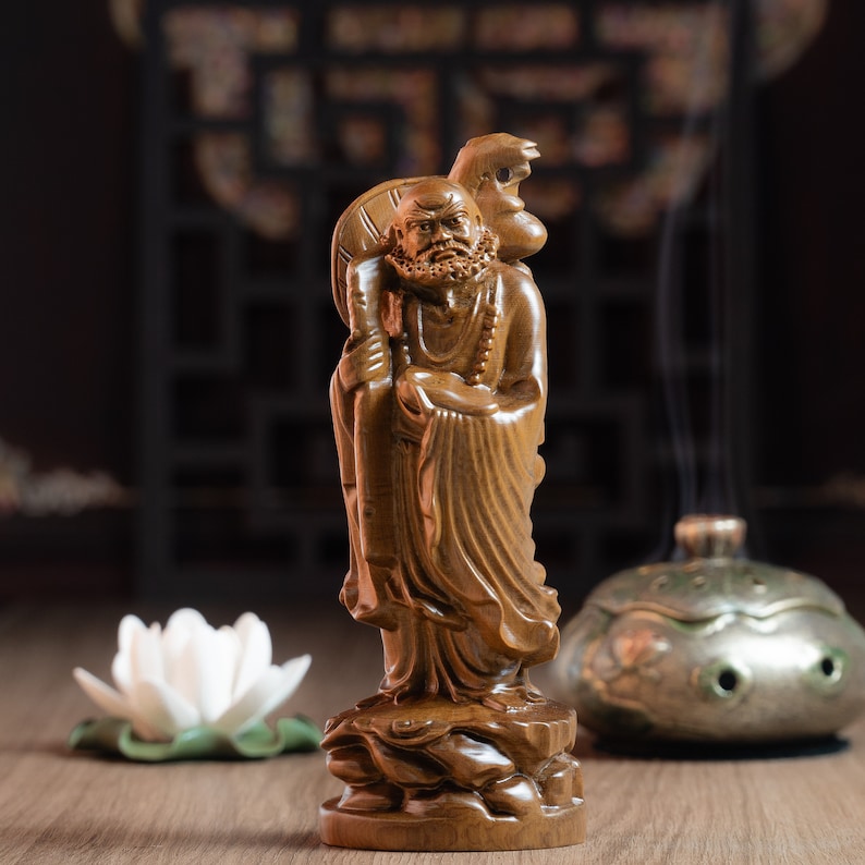 May include: A wooden statue of a man with a long beard and a staff, holding a small animal on his shoulder. The statue is standing on a base with a carved design. The statue is brown and has a natural wood finish.