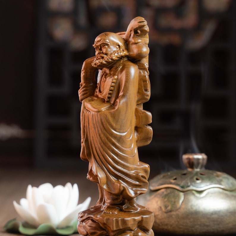 May include: A wooden sculpture of a man with a long beard and a staff. The sculpture is carved in a detailed style and has a warm brown color.