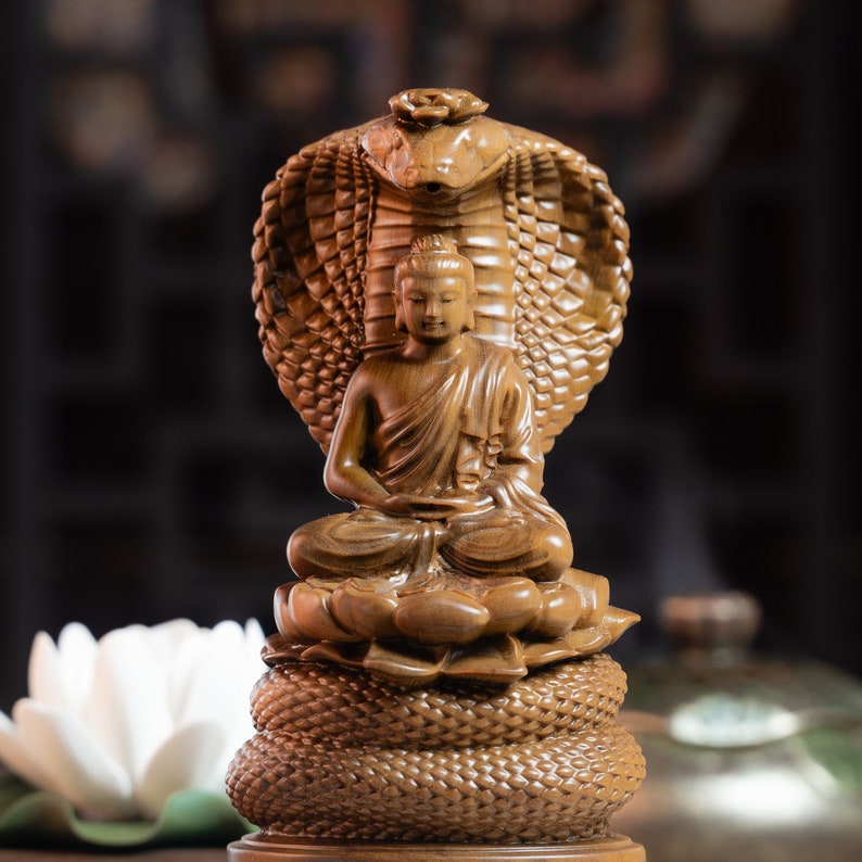 May include: A wooden sculpture of Buddha seated in meditation, with a cobra hood behind him. The sculpture is intricately carved and has a warm brown colour.