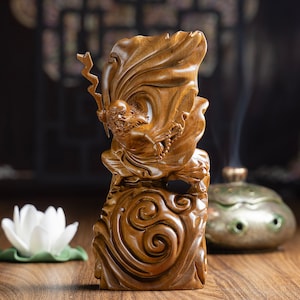 May include: A wooden sculpture of a figure with a flowing robe, standing on a cloud-like base. The figure is carved in a detailed style, with intricate details in the clothing and facial features. The sculpture is made of a light brown wood and has a natural finish.