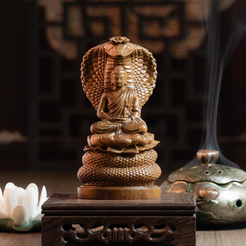 May include: A wooden statue of Buddha seated in meditation, with a cobra hood behind him. The statue is on a wooden base and is surrounded by incense smoke.