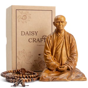 May include: A wooden statue of a seated monk with hands clasped in prayer, a wooden bead necklace, and a cardboard box. The box features the text "DAISY CRAFT" and lotus flower illustrations. The statue and beads are brown.