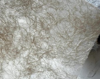 May include: Close-up of textured, off-white paper with a network of fine, brown fibres. The paper has a crinkled appearance, with subtle variations in tone and texture. The fibres create a delicate, organic pattern across the surface.