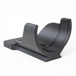 Op de afbeelding: Een zwarte plastic metaaldetectorstandaard met een gebogen wieg en een rechthoekige basis. De standaard is ontworpen om een metaaldetector vast te houden en is gemaakt van duurzaam plastic.