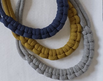 Puede incluir: Tres collares de cuerda anudados en gris, amarillo mostaza y azul marino. Los collares están superpuestos.