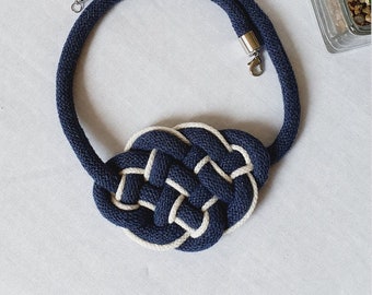 Puede incluir: Un collar de cuerda azul marino con un nudo de cuerda blanco. El collar tiene un cierre plateado.