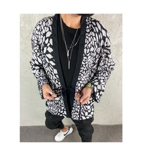 May include: A black and white animal print kimono with a black trim and a tie belt. The kimono is worn over a black t-shirt and black pants.
