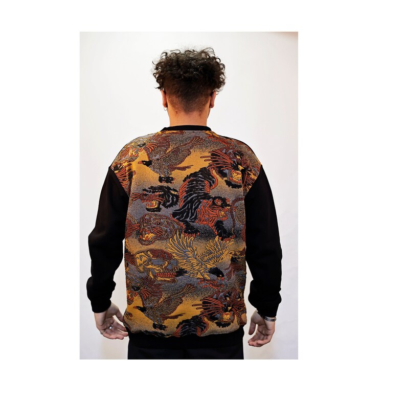 May include: A black long-sleeved sweater with a colourful print of birds and animals on the back. The print features a gold, orange, and blue colour scheme.