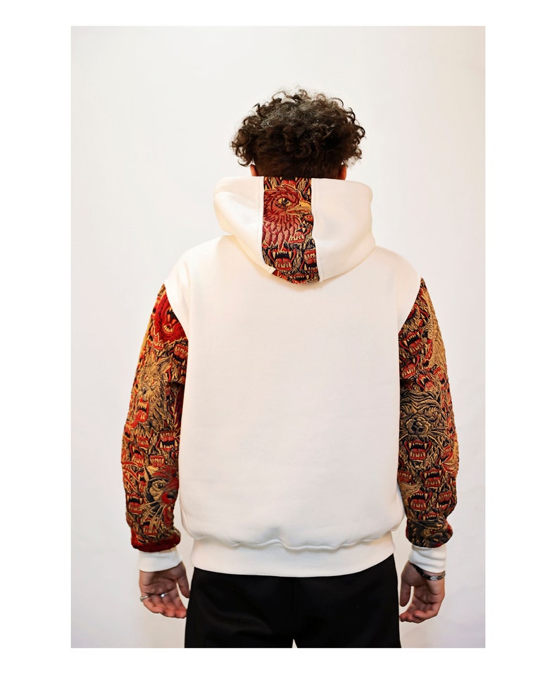 May include: White hooded sweatshirt with a red and gold patterned design on the back and sleeves. The pattern features a repeated image of a lion's head.