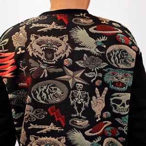 Puede incluir: Sudadera negra con un estampado colorido de varios s&iacute;mbolos y dise&ntilde;os, incluyendo una calavera, una estrella, un p&aacute;jaro y un tigre.
