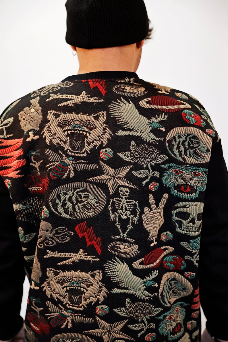 Puede incluir: Sudadera negra con un estampado colorido de varios s&iacute;mbolos y dise&ntilde;os, incluyendo una calavera, una estrella, un p&aacute;jaro y un tigre.