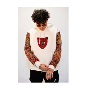 May include: A white hoodie with a red bear face embroidered on the front. The sleeves are patterned with a brown and red design.