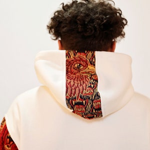 May include: White hooded sweatshirt with a red, gold, and blue tapestry design on the back of the hood.