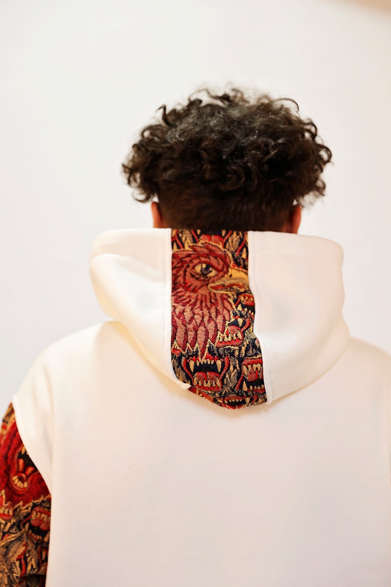 May include: White hooded sweatshirt with a red, gold, and blue tapestry design on the back of the hood.