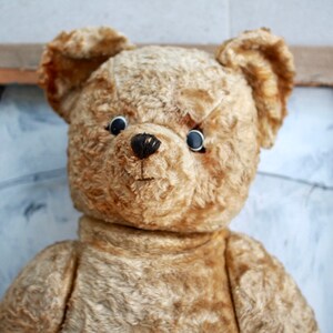 Peut inclure: Un ours en peluche vintage avec un pelage us&eacute; de couleur fauve et des yeux en boutons noirs. L'ours a un nez cousu et une expression douce, l&eacute;g&egrave;rement triste.