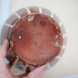 K&ouml;nnte beinhalten: Eine braune Keramikvase mit einem gelben und wei&szlig;en Streifenmuster. Die Vase hat einen runden Boden und eine breite &Ouml;ffnung.