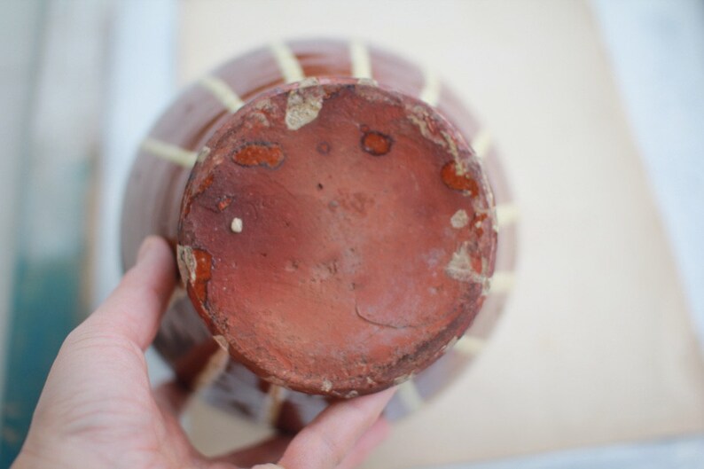 K&ouml;nnte beinhalten: Eine braune Keramikvase mit einem gelben und wei&szlig;en Streifenmuster. Die Vase hat einen runden Boden und eine breite &Ouml;ffnung.