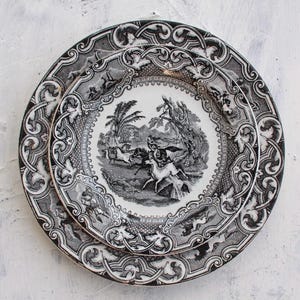 May include: A set of three black and white porcelain plates with intricate floral designs. The centre plate features a black and white illustration of a hunting scene with horses and riders.