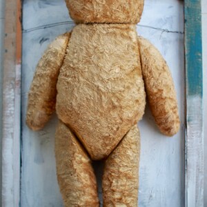 Peut inclure: Un ours en peluche vintage avec un pelage us&eacute; de couleur fauve. L'ours est debout dans un cadre en bois sur un fond blanc.