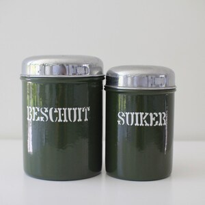 Pode incluir: Dois recipientes de metal verde vintage com tampas prateadas. O recipiente à esquerda diz "BESCHUIT" e o recipiente à direita diz "SUIKER".
