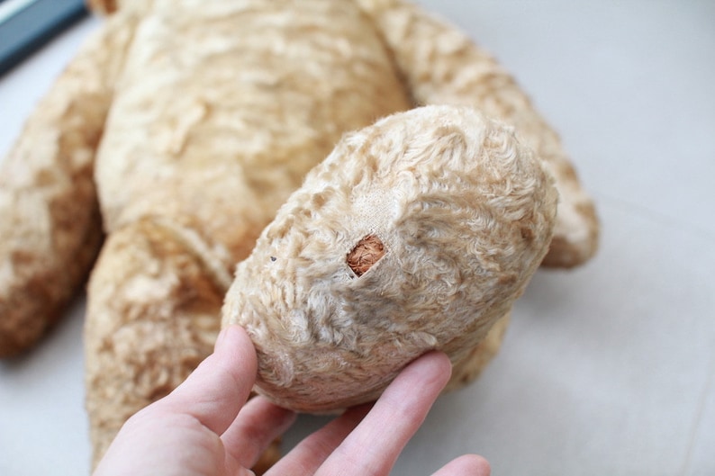 Peut inclure: Un ours en peluche vintage de couleur cr&egrave;me avec un morceau de tissu us&eacute; sur sa patte. La fourrure de l'ours est moelleuse et a un aspect d&eacute;lav&eacute;.