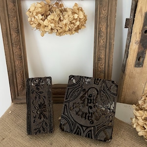 May include: Two vintage wooden printing blocks with intricate floral and geometric designs. The blocks are dark brown and have a worn, antique look.