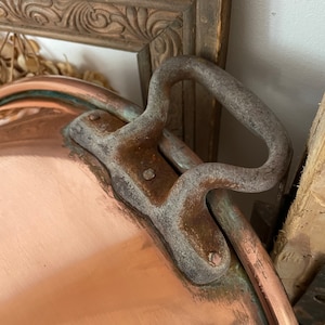 Puede incluir: Una olla grande de cobre con un asa de hierro resistente. La olla tiene una p&aacute;tina desgastada y envejecida y probablemente sea vintage.