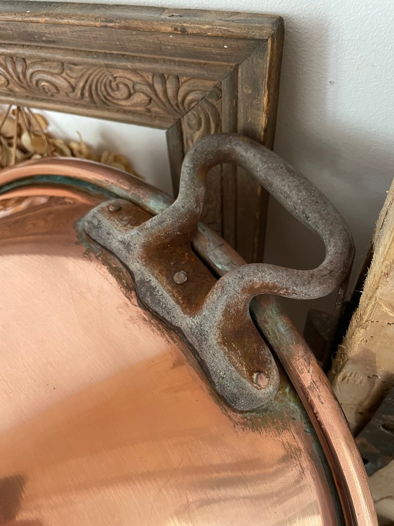Puede incluir: Una olla grande de cobre con un asa de hierro resistente. La olla tiene una p&aacute;tina desgastada y envejecida y probablemente sea vintage.