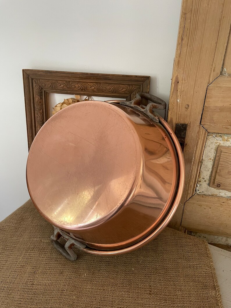 Puede incluir: Una olla grande de cobre con dos asas de hierro. La olla es brillante y tiene un aspecto desgastado y envejecido.