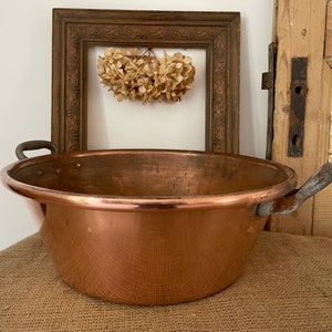 Puede incluir: Una olla grande de cobre con dos asas de hierro. La olla est&aacute; sobre una superficie de arpillera.