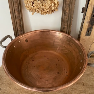Puede incluir: Una olla grande de cobre con dos asas. La olla est&aacute; vac&iacute;a y tiene un acabado brillante y met&aacute;lico.