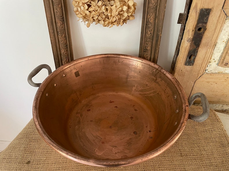 Puede incluir: Una olla grande de cobre con dos asas. La olla est&aacute; vac&iacute;a y tiene un acabado brillante y met&aacute;lico.