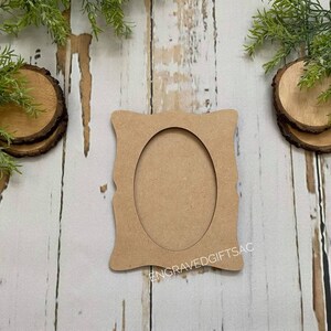 May include: A plain, unfinished, oval-shaped picture frame made of wood. The frame has a decorative, scalloped edge. The frame is sitting on a white wooden surface. The text "ENGRAVEDGIFTSAC" is printed on the bottom of the frame.