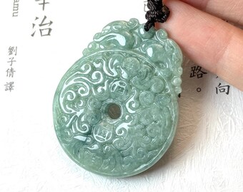 Puede incluir: Un colgante de jade verde con un diseño de dragón y un agujero redondo en el centro. El colgante está en un collar de cordón negro.