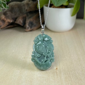May include: A jade green pendant necklace featuring a detailed carving of a rooster. The pendant is attached to a silver chain.