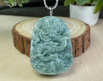May include: A jade green pendant featuring a detailed carving of a dragon. The pendant is attached to a silver chain.