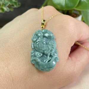 May include: A jade green pendant necklace featuring a carved rooster design. The pendant is attached to a gold chain.