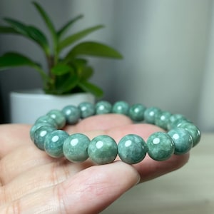May include: A green jade stone bracelet with round beads. The bracelet is on a person's hand.