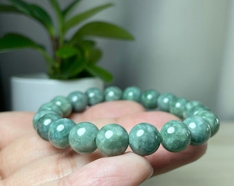 Puede incluir: Un brazalete de jade verde con cuentas redondas. El brazalete está en la mano de una persona.