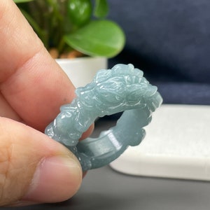 May include: A jade ring featuring a carved dragon design. The ring is a pale green colour and has a smooth, polished finish.