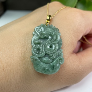 May include: A jade green dragon pendant carved from jade with intricate details. The pendant is attached to a gold chain.