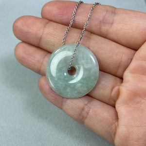 May include: A green jade pendant in the shape of a donut, hanging from a silver chain.